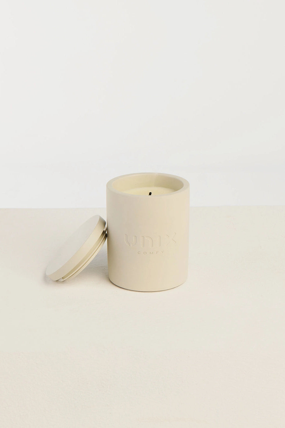 Grey scented candle close up UNIX logo embossed minimalist - UNIX | شمعة معطرة رمادية لقطة قريبة بلوجو UNIX بارز بتصميم بسيط - UNIX